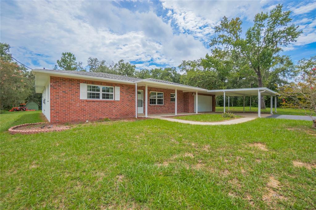 A single-story red brick house features a front porch, attached garage, and a metal carport — 1919 FOREST DRIVE, INVERNESS, FL