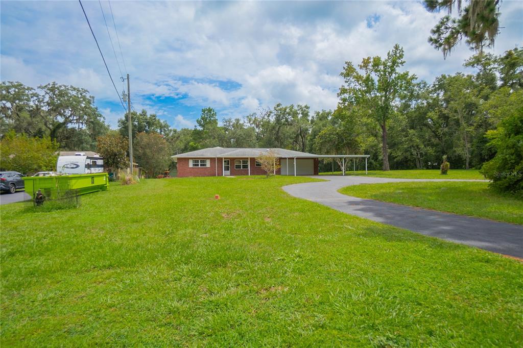 A single-story brick house with a carport sits on a large, grassy lot — 1919 FOREST DRIVE, INVERNESS, FL