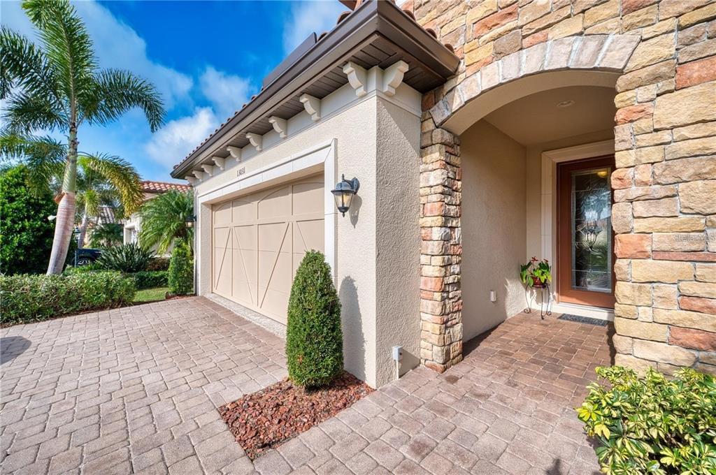 A stone-accented home exterior features a beige garage door, a paved driveway, and a palm tree — 13031 PALERMO DRIVE, BRADENTON, FL