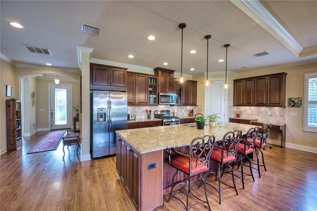 A kitchen features dark wood cabinets, granite countertops, a large island, and three pendant lights — 13031 PALERMO DRIVE, BRADENTON, FL
