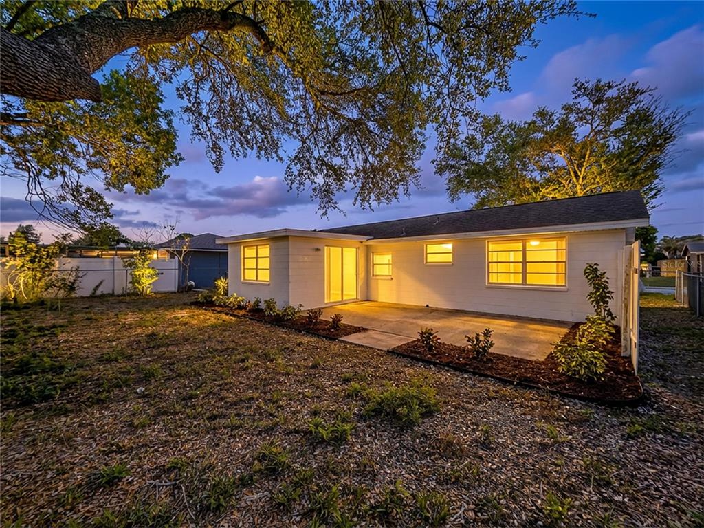 The exterior of a white house features a concrete patio and a large tree — 9741 LAMANTIN DRIVE, PORT RICHEY, FL
