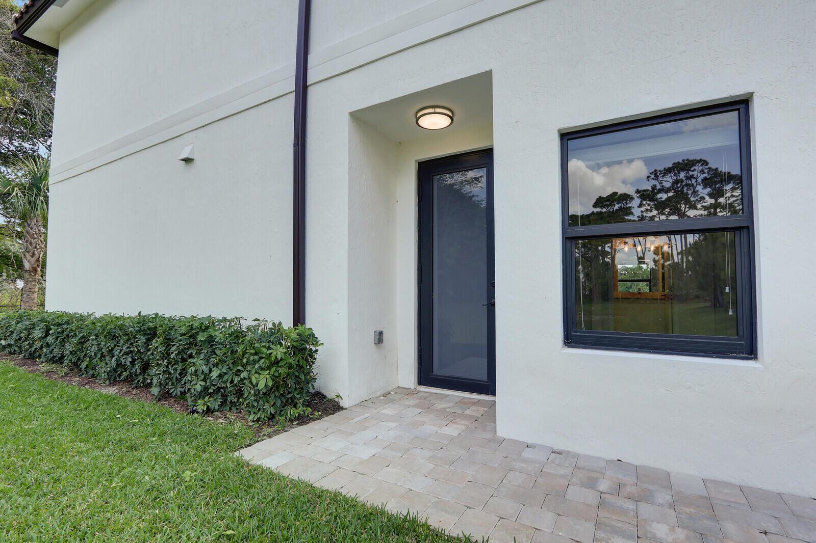 A white exterior wall features a dark-framed door, a window, and a paved walkway — 406 Bella Sol Way, West Palm Beach FL 33406, WEST PALM BEACH, FL