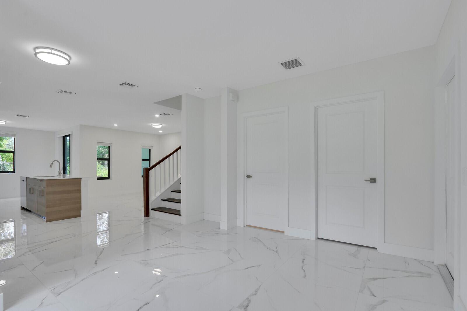 A bright, open-concept room features white marble flooring, a kitchen island, and a wooden staircase — 406 Bella Sol Way, West Palm Beach FL 33406, WEST PALM BEACH, FL