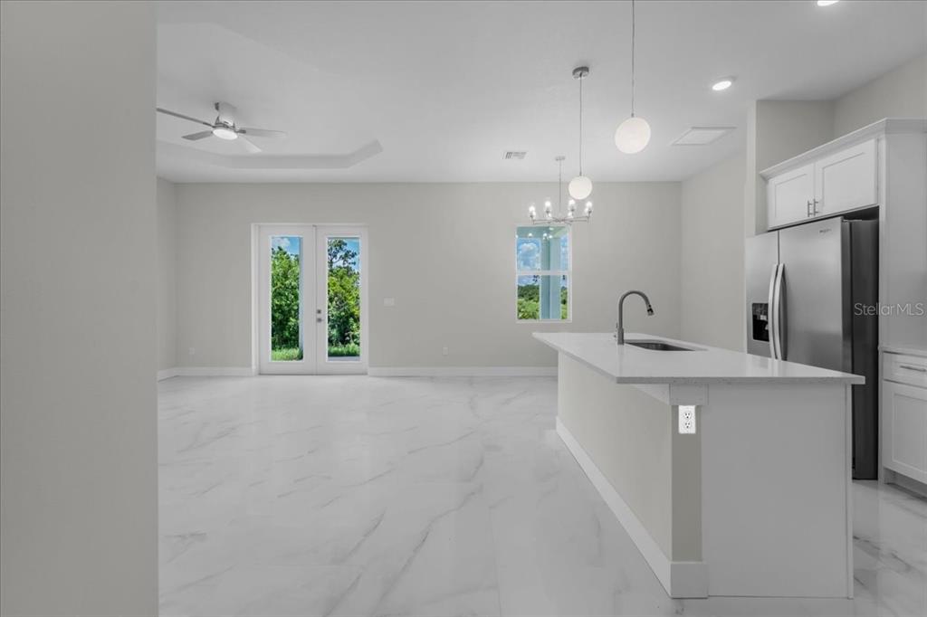 A modern kitchen with a white island and marble-style flooring opens to a living area — 1911 RICHMOND AVENUE N, LEHIGH ACRES, FL