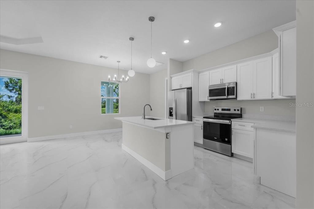 A modern kitchen features white cabinetry, a central island, and light-colored marble-look tile flooring — 1911 RICHMOND AVENUE N, LEHIGH ACRES, FL