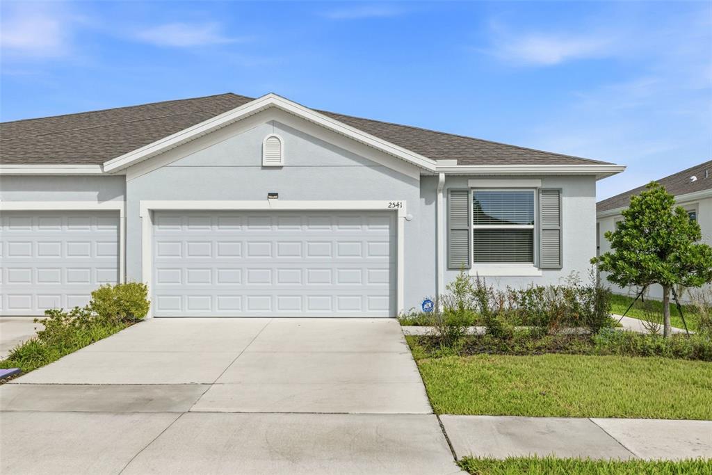 A light blue single-story house exterior features a two-car garage and a front window — 2541 BENDING BONSAI DRIVE, WESLEY CHAPEL, FL