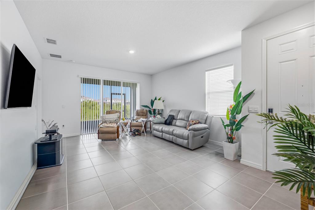 A living room with light tile flooring, a gray sofa, two recliners, and sliding glass doors — 2541 BENDING BONSAI DRIVE, WESLEY CHAPEL, FL