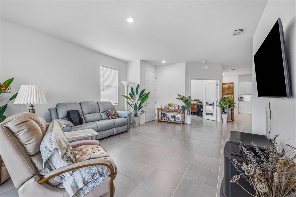 A living room features gray tile flooring, a gray sofa, a recliner, and a television — 2541 BENDING BONSAI DRIVE, WESLEY CHAPEL, FL