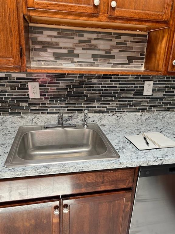 A kitchen sink with a granite countertop and a tiled backsplash sits below wooden cabinets — 53 21ST TERRACE SE, LARGO, FL