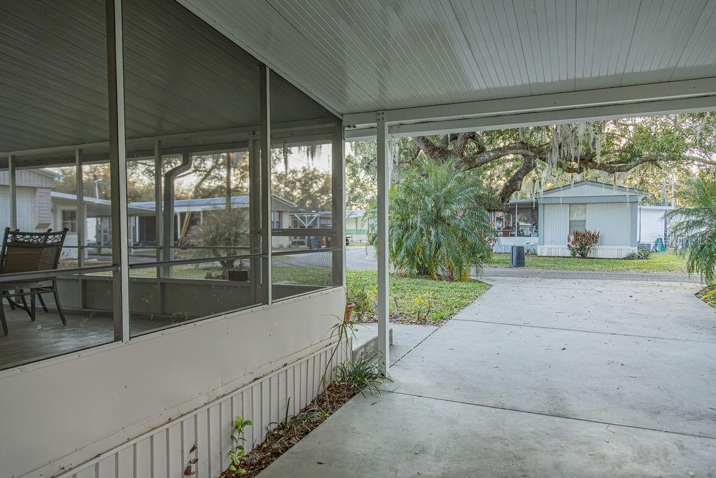 A screened-in porch overlooks a concrete driveway and a neighboring mobile home — 23 ANCHOR INN ROAD, LAKE WALES, FL