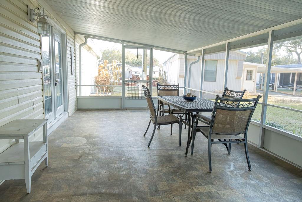 A screened-in porch with a tiled floor, dining set, and views of neighboring homes — 23 ANCHOR INN ROAD, LAKE WALES, FL