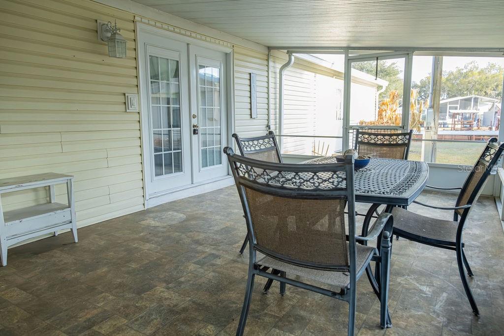 A screened-in porch features a dining set, tiled flooring, and white French doors — 23 ANCHOR INN ROAD, LAKE WALES, FL