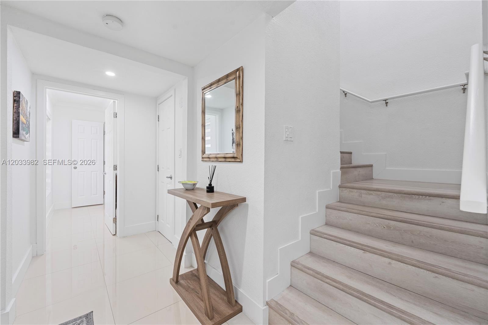 A bright entryway features a wooden console table, a mirror, and stairs with light wood treads — 9780 SW 19th St, Miami FL 33165, MIAMI, FL