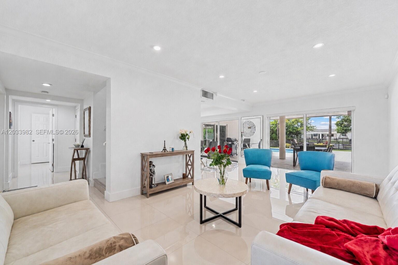 A bright living room features white tile floors, two blue chairs, and a sliding glass door — 9780 SW 19th St, Miami FL 33165, MIAMI, FL