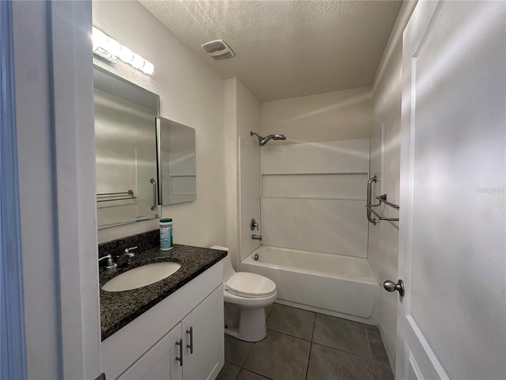 A bathroom features a vanity with a dark countertop, a toilet, and a shower-tub combo — 1454 MARY BELLE AVENUE, KISSIMMEE, FL