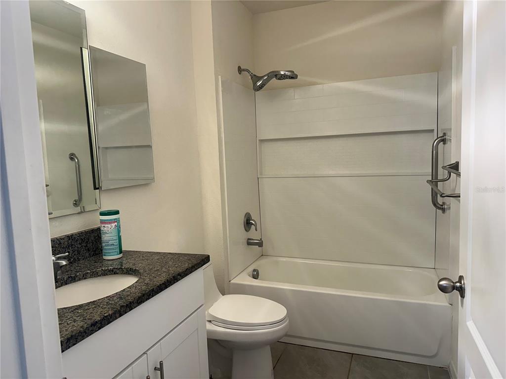 A bathroom features a white vanity with a granite countertop, a toilet, and a tub-shower — 1454 MARY BELLE AVENUE, KISSIMMEE, FL