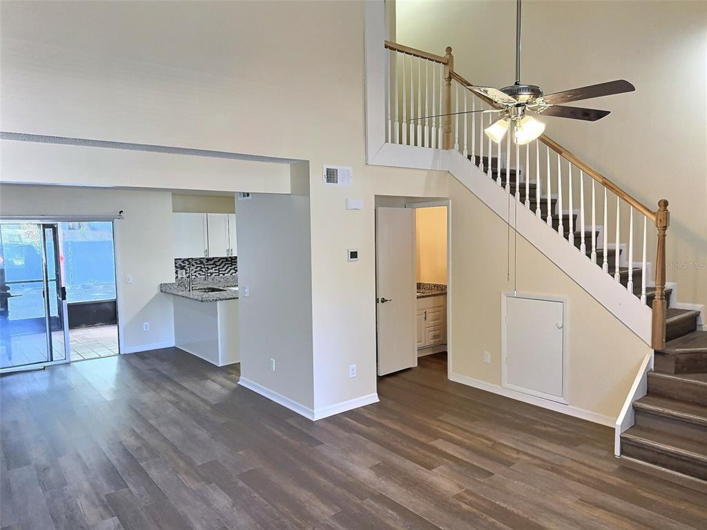 A living area with wood-look flooring, a staircase, and an adjacent kitchen with white cabinets — 1257 WINTER GREEN WAY, WINTER GARDEN, FL