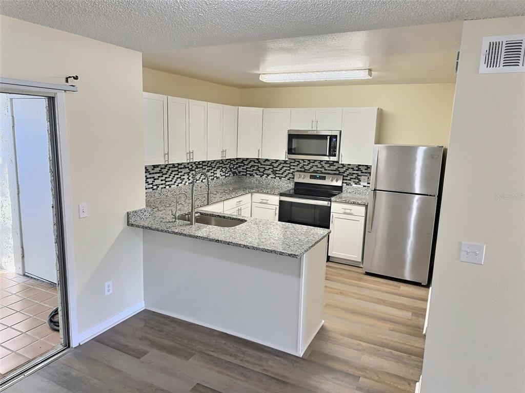 A kitchen features white cabinets, granite countertops, stainless steel appliances, and wood-look flooring — 1257 WINTER GREEN WAY, WINTER GARDEN, FL