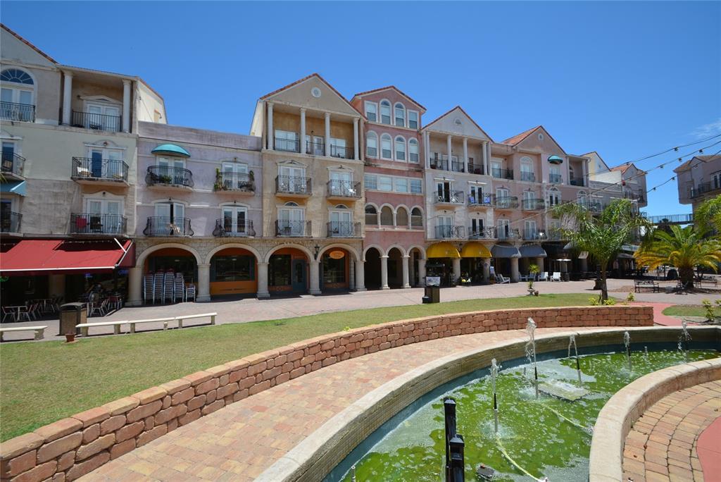 A multi-story building with balconies and arched storefronts overlooks a brick-lined fountain and lawn — 101 PALM HARBOR PARKWAY UNIT A202, PALM COAST, FL