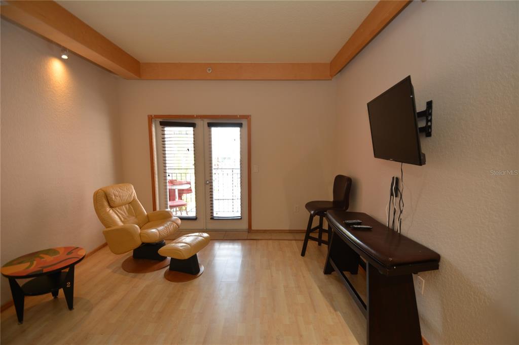 A living room with light wood flooring, a leather recliner, a wall-mounted television, and balcony doors — 101 PALM HARBOR PARKWAY UNIT A202, PALM COAST, FL