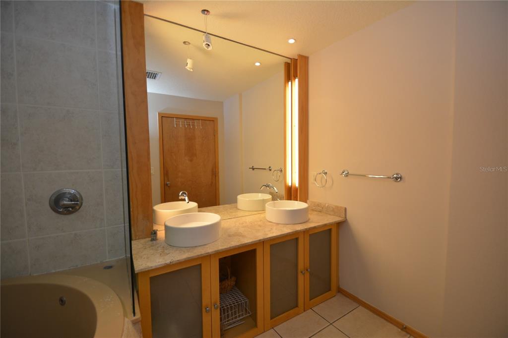 A bathroom features a double vanity with vessel sinks, a large mirror, and a soaking tub — 101 PALM HARBOR PARKWAY UNIT A202, PALM COAST, FL