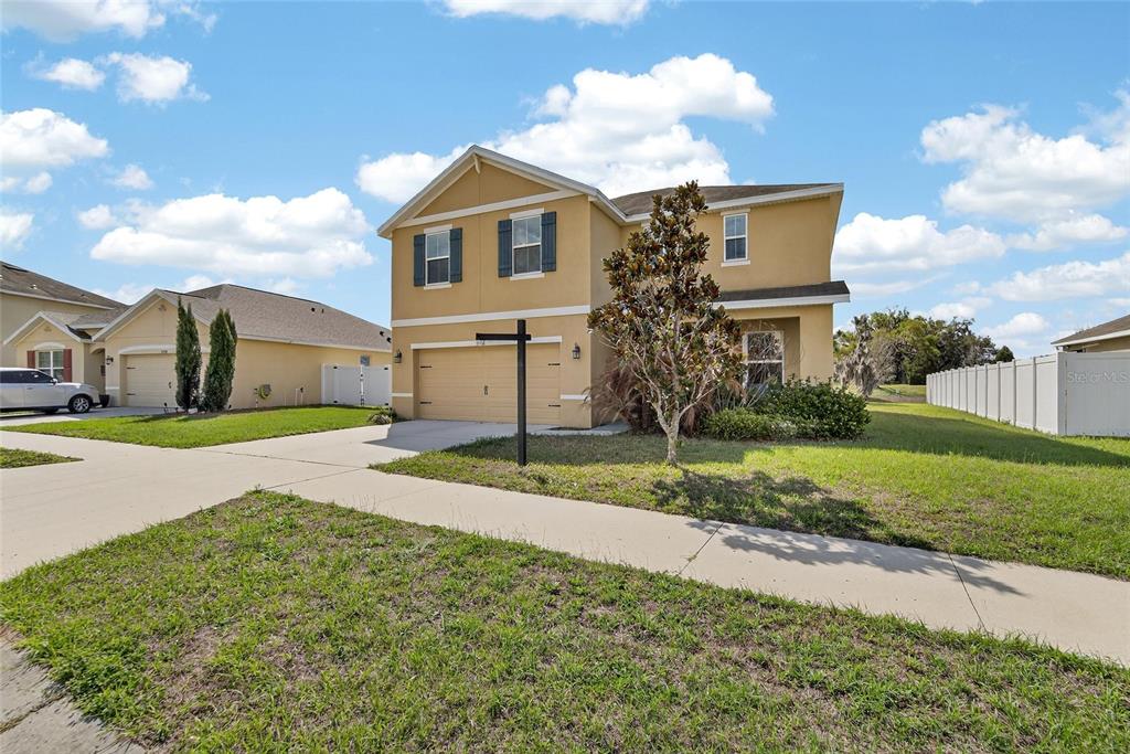 A two-story tan house with a two-car garage and a white vinyl fence — 35716 HILLBROOK AVENUE, ZEPHYRHILLS, FL