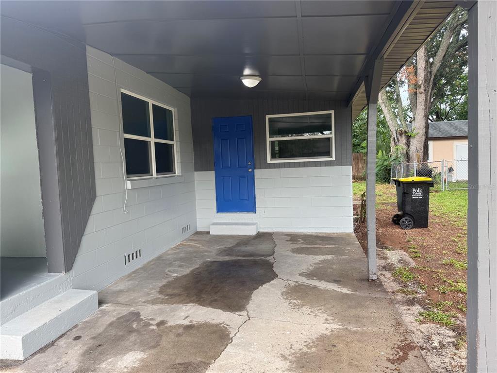 A covered concrete patio features a blue door, gray block walls, and a trash bin — 309 1ST STREET, AUBURNDALE, FL