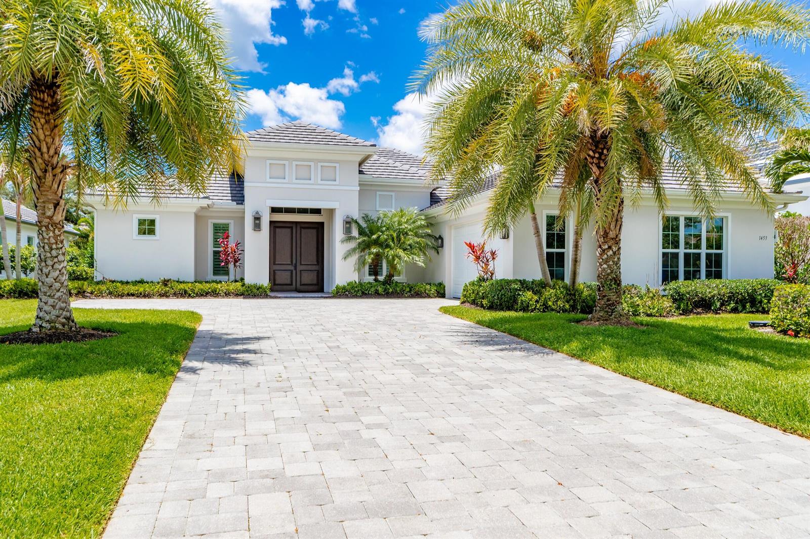 A single-story house with a paved driveway, palm trees, and a dark double-door entrance — VERO BEACH, FL