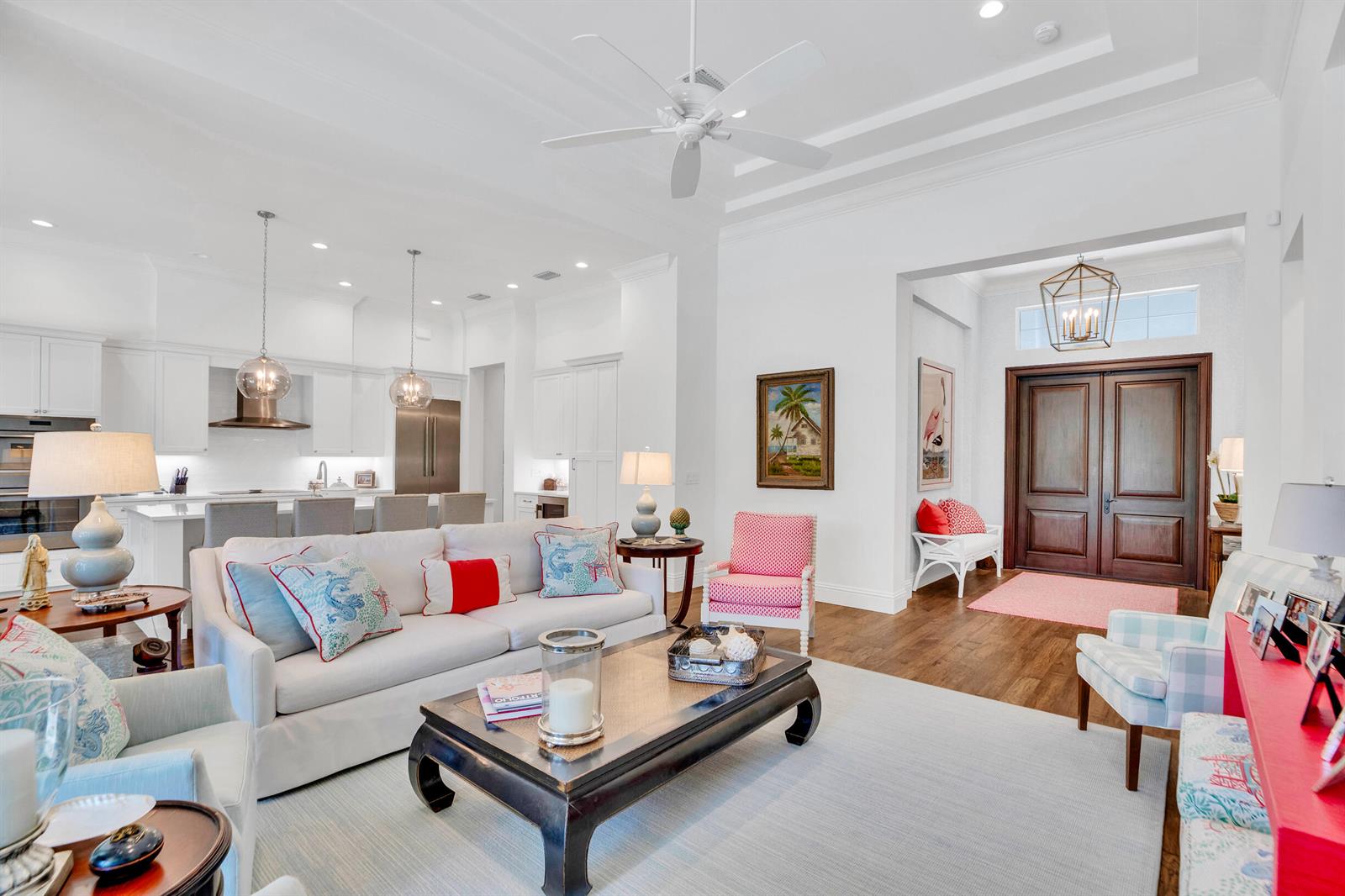 A bright, open-concept living room and kitchen featuring white cabinetry, hardwood floors, and coastal decor — VERO BEACH, FL