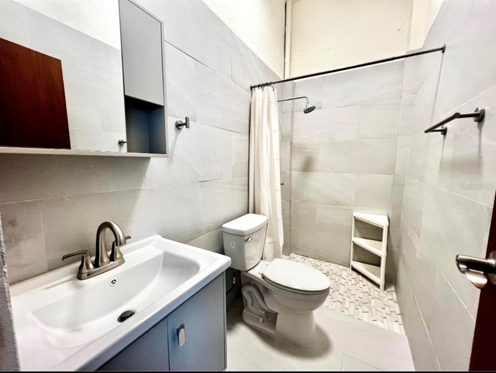 A bathroom features a vanity, a toilet, and a tiled walk-in shower with a curtain — 119 STA CECILIA, SAN JUAN, PR