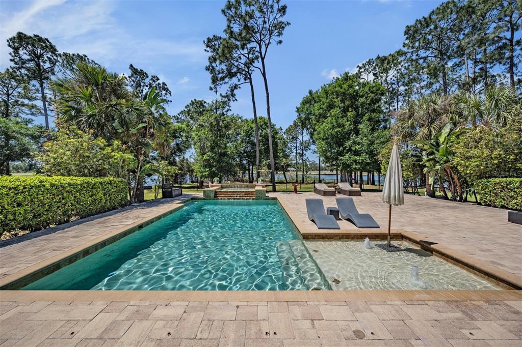 A rectangular swimming pool with a tanning ledge and spa sits on a stone patio — 9134 TILLINGHAST DRIVE, TAMPA, FL