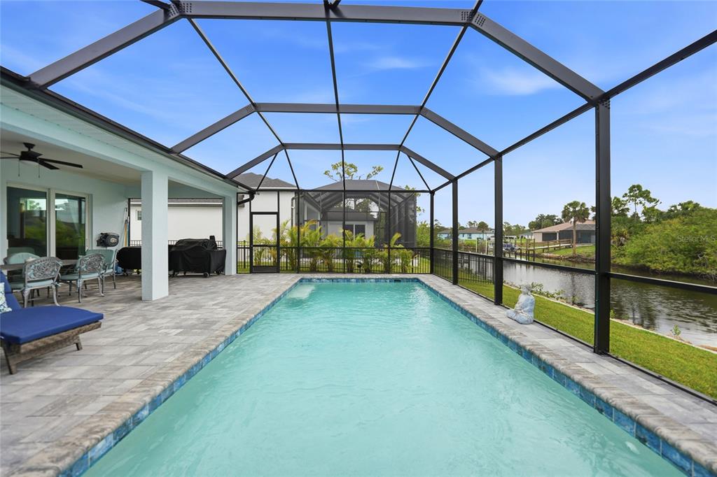 A screened-in patio features a rectangular swimming pool, stone pavers, and a view of water — 1411 LIGGETT CIRCLE, PORT CHARLOTTE, FL