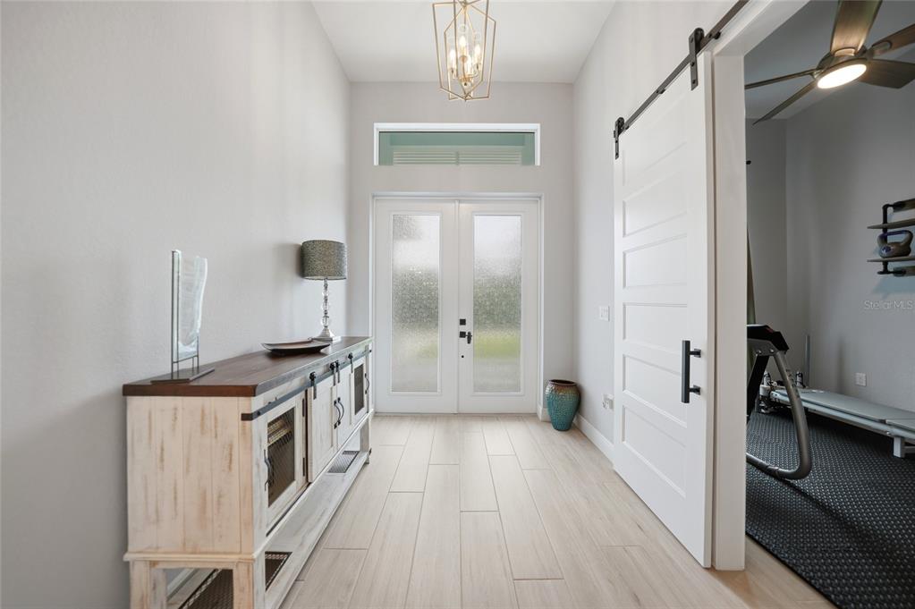 A bright entryway features light wood-look tile floors, a white barn door, and double front doors — 1411 LIGGETT CIRCLE, PORT CHARLOTTE, FL
