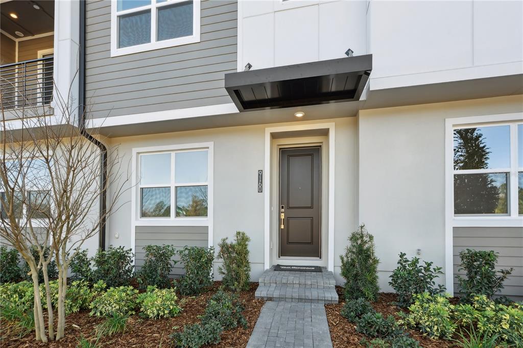 The exterior of a modern townhome features a dark front door, gray siding, and landscaping — 9160 SINATRA LANE, ORLANDO, FL