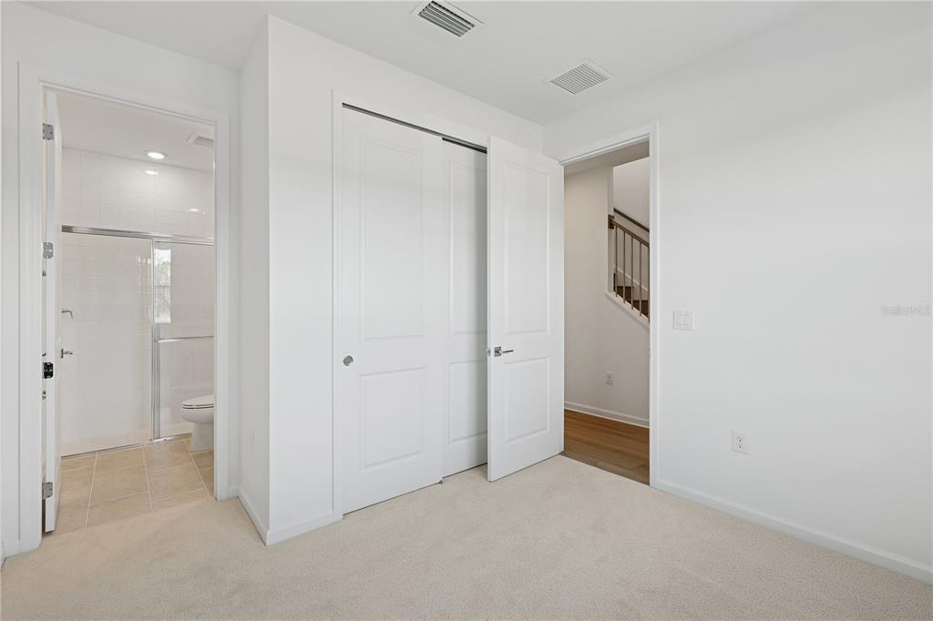 A bedroom features beige carpet, a white closet, and an adjacent bathroom with a shower — 9160 SINATRA LANE, ORLANDO, FL