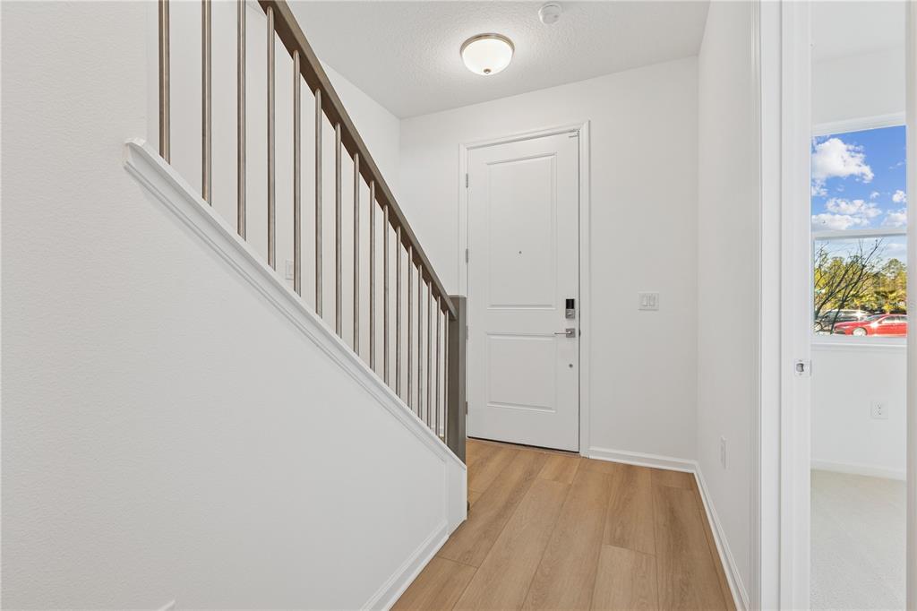 An entryway features light wood flooring, a white door, and a staircase with metal railings — 9160 SINATRA LANE, ORLANDO, FL