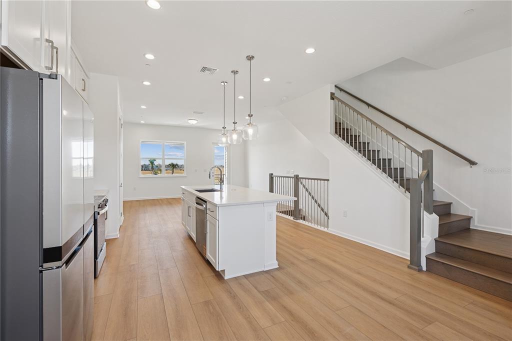 A modern kitchen features white cabinets, a central island, and stairs with dark wood treads — 9160 SINATRA LANE, ORLANDO, FL