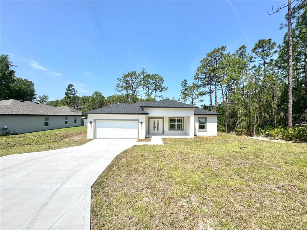 A single-story white house with a two-car garage sits on a grassy lot with trees — 7578 N PRIMROSE DRIVE, CITRUS SPRINGS, FL