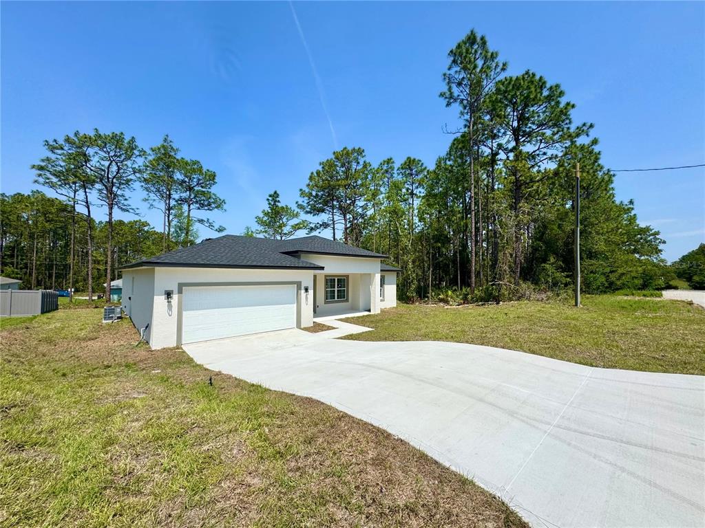 A single-story house with a white exterior, dark roof, and concrete driveway sits among trees — 7578 N PRIMROSE DRIVE, CITRUS SPRINGS, FL