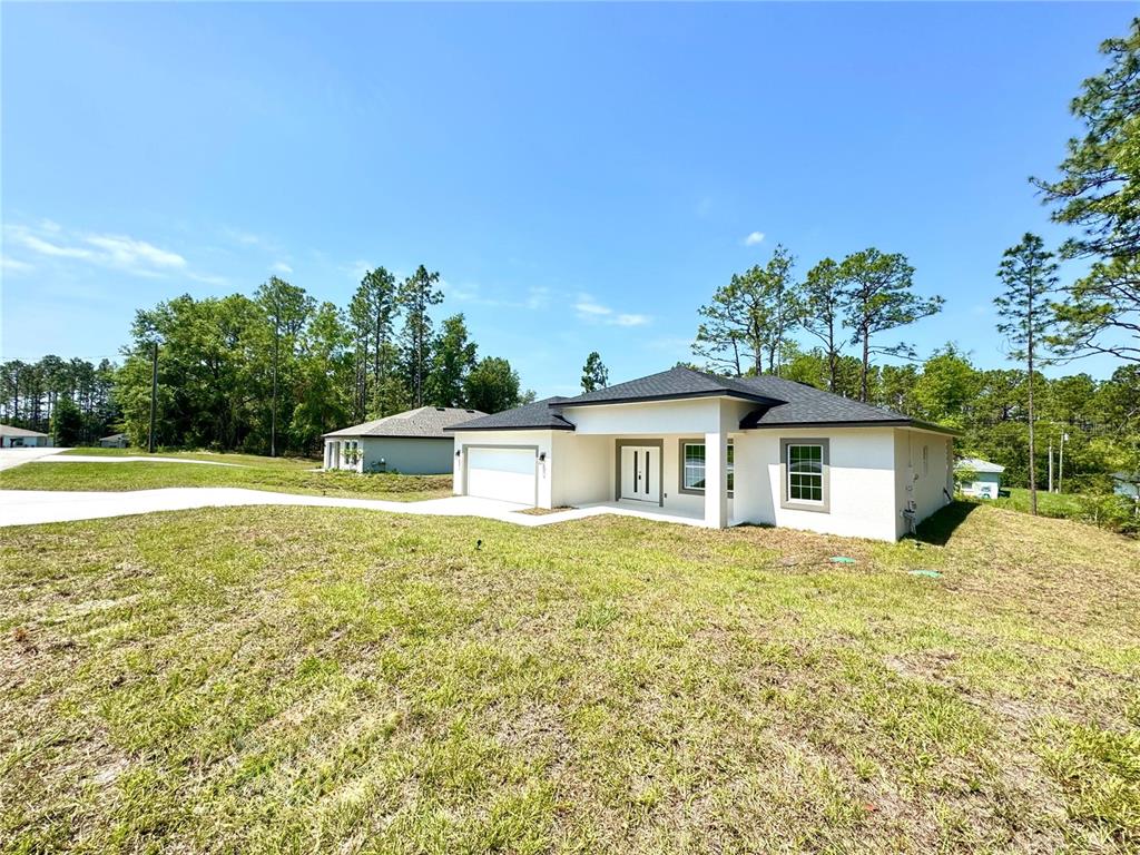 A single-story white house with a dark roof and attached garage sits on a grassy lot — 7578 N PRIMROSE DRIVE, CITRUS SPRINGS, FL
