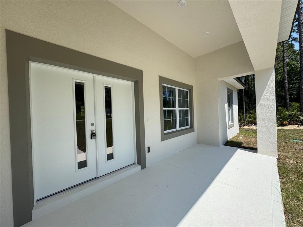 A covered concrete porch features a white double front door and a single window — 7578 N PRIMROSE DRIVE, CITRUS SPRINGS, FL