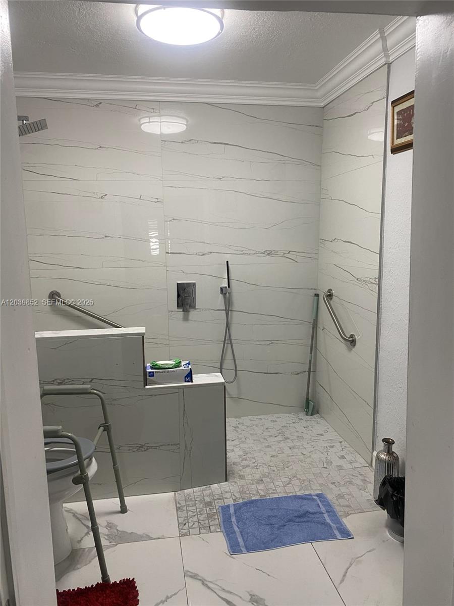 A walk-in shower features white marble-look tile walls, a mosaic floor, and grab bars — MARGATE, FL