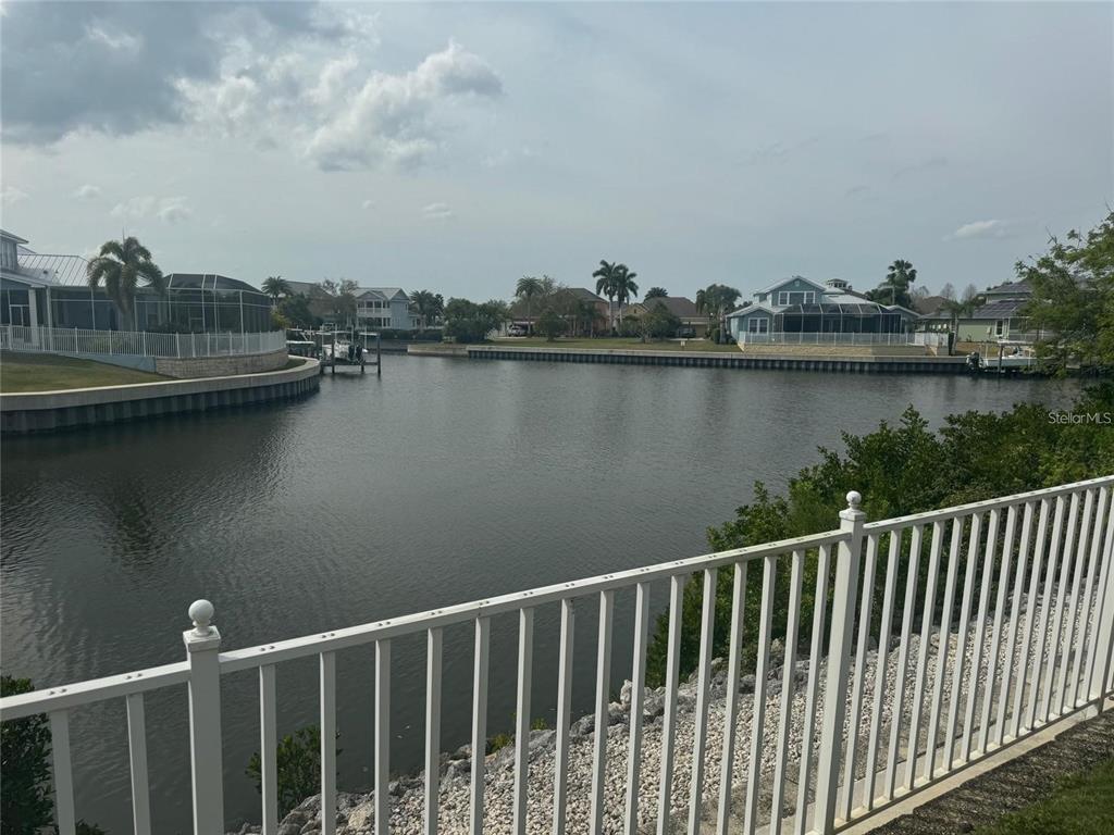 A white fence overlooks a canal lined with houses and boat docks under a cloudy sky — 5714 TIDES PLACE, APOLLO BEACH, FL