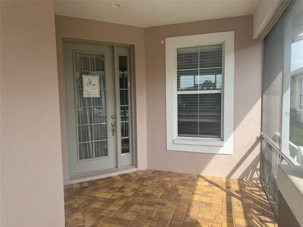 A covered porch features tan brick pavers, a light green front door, and a window — 5714 TIDES PLACE, APOLLO BEACH, FL
