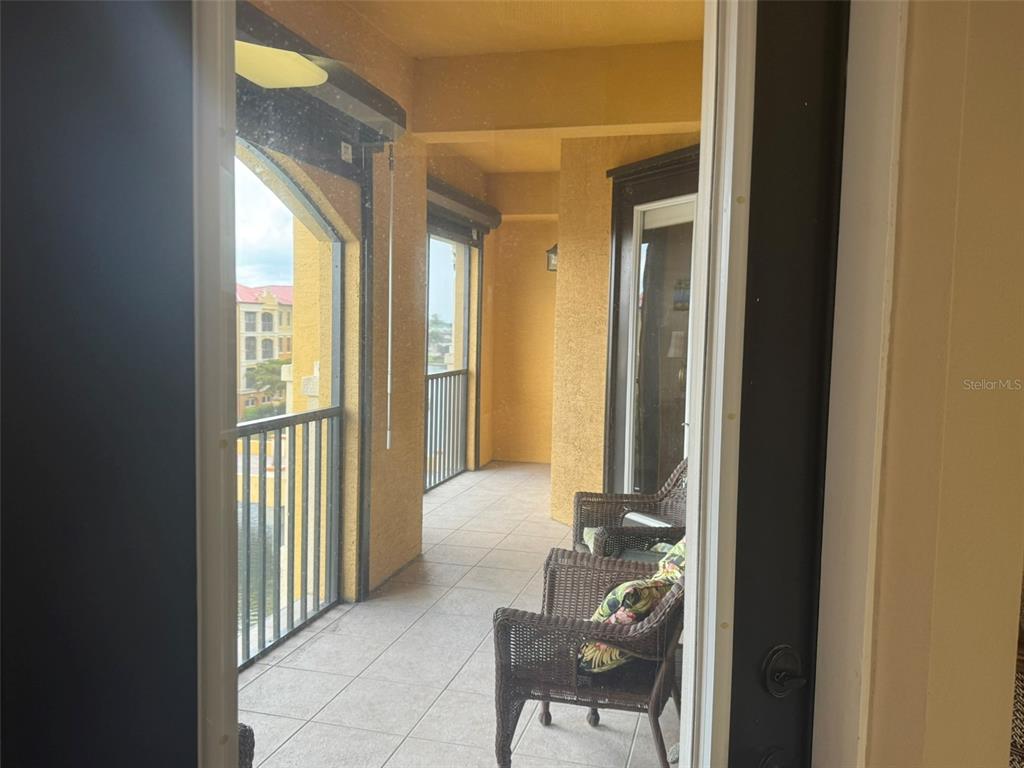 A covered balcony features tiled flooring, wicker chairs, and metal railings overlooking a building exterior — 99 VIVANTE BOULEVARD UNIT 415, PUNTA GORDA, FL