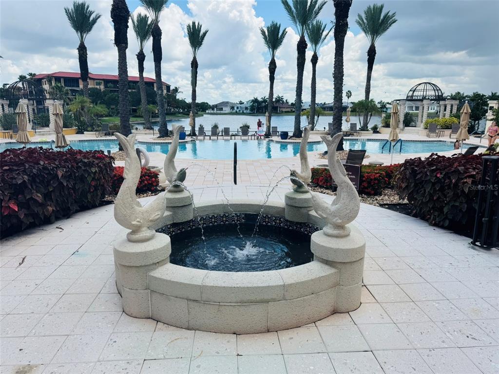 A stone fountain with dolphin sculptures sits on a patio overlooking a swimming pool — 99 VIVANTE BOULEVARD UNIT 415, PUNTA GORDA, FL