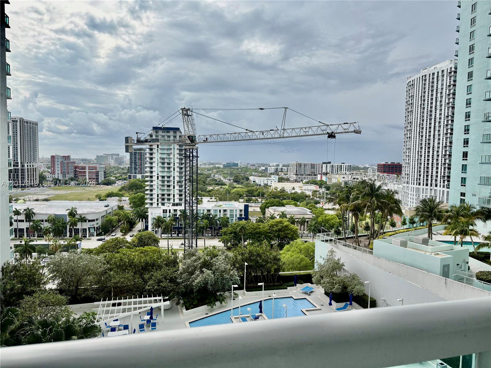 An elevated view shows a swimming pool, lush trees, and a construction crane in a city — 1800 N Bayshore Dr # 1704, Miami FL 33132, MIAMI, FL