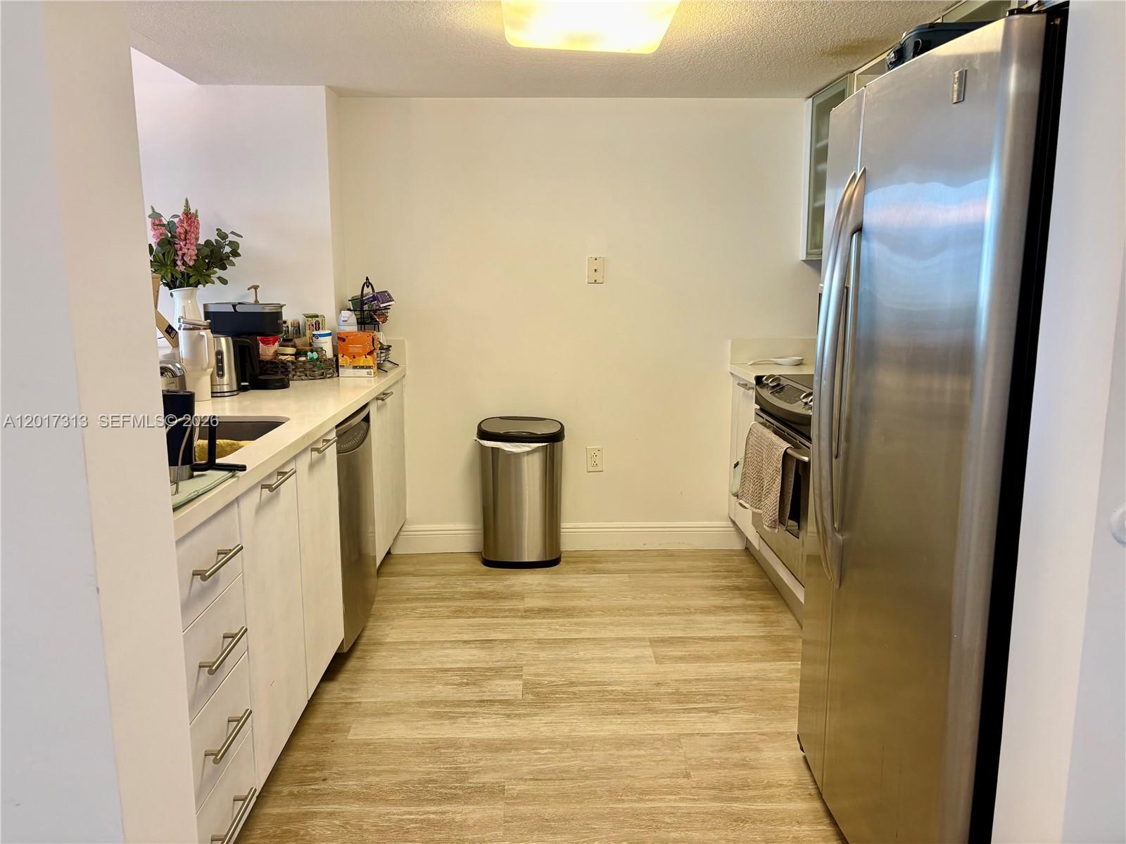 A galley kitchen features white cabinets, stainless steel appliances, and light wood-look flooring — 1800 N Bayshore Dr # 1704, Miami FL 33132, MIAMI, FL