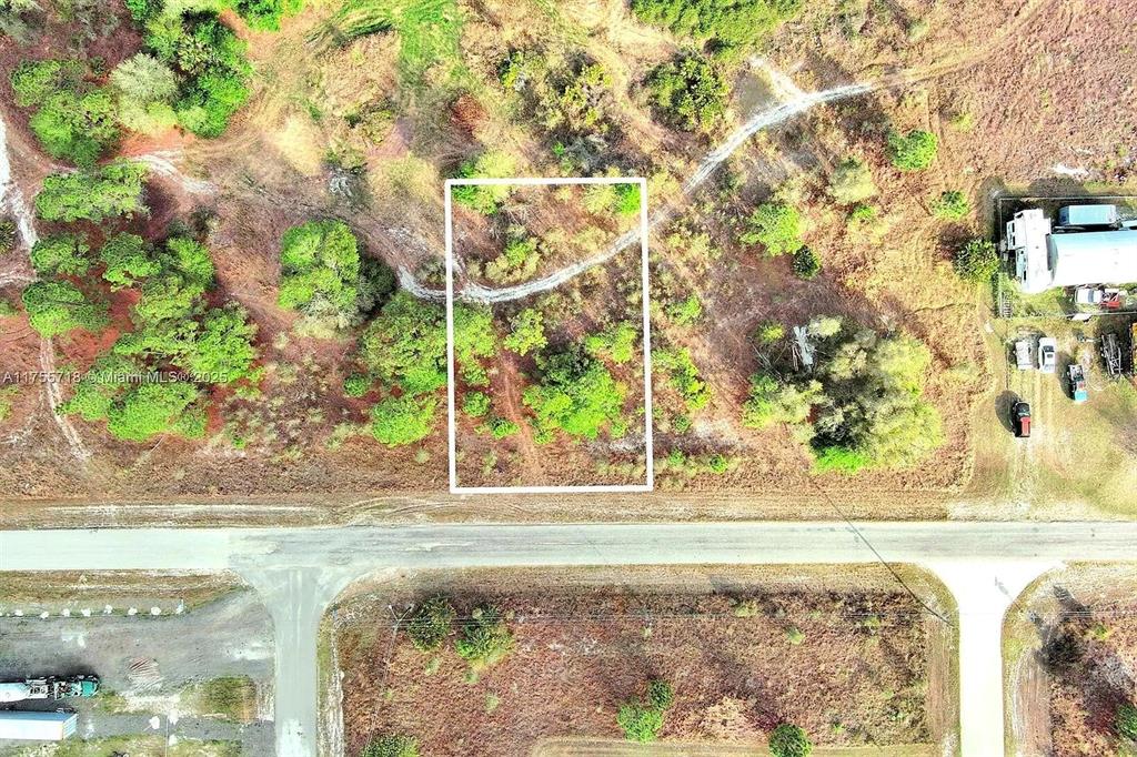 An aerial view shows a rectangular plot of land outlined in white near a road — 565 SUMMIT AVENUE S, LEHIGH ACRES, FL