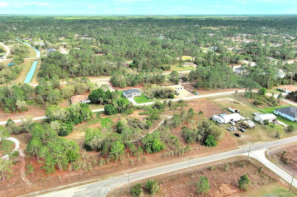 An aerial view shows a rural residential area with scattered houses, wooded lots, and roads — 565 SUMMIT AVENUE S, LEHIGH ACRES, FL